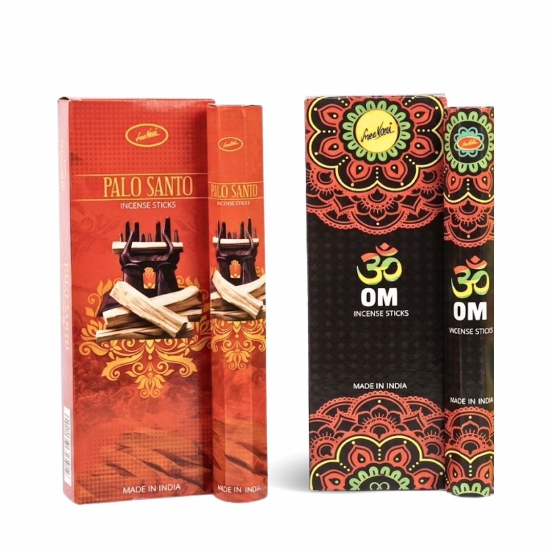Dos cajas de varitas de incienso Sree Vani de pie contra un fondo blanco. La caja de la izquierda es roja con detalles dorados, presenta la ilustración de unos leños de Palo Santo y la marca "Sree Vani". La caja de la derecha es negra con un patrón de mandala naranja y amarillo, el símbolo "OM" y la marca "Sree Vani". Ambas cajas dicen "HECHO EN INDIA".