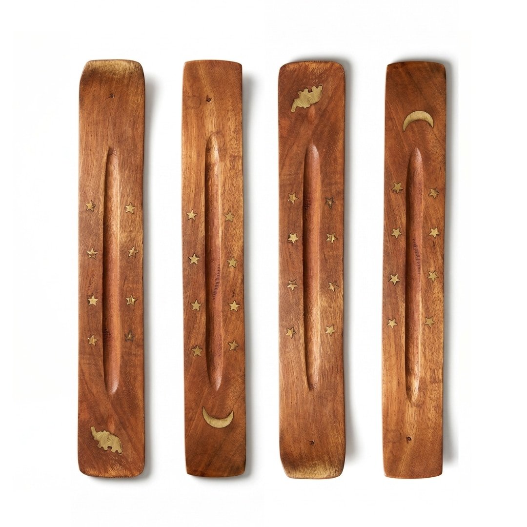 Dos porta inciensos de madera pulida en forma de canoa, uno decorado con una luna creciente y estrellas de latón, y el otro con un elefante y estrellas, sobre un fondo blanco puro.