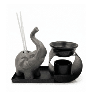 Set de aromaterapia que incluye un elefante de cerámica gris con varillas, un cuenco difusor negro sobre soporte metálico y una bandeja de metal negra sobre fondo blanco.
