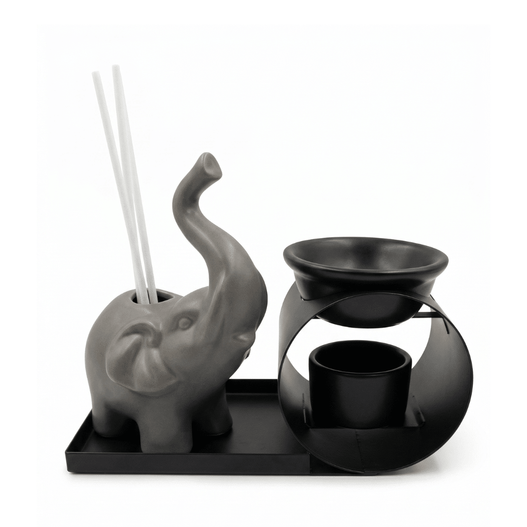 Set de aromaterapia que incluye un elefante de cerámica gris con varillas, un cuenco difusor negro sobre soporte metálico y una bandeja de metal negra sobre fondo blanco.