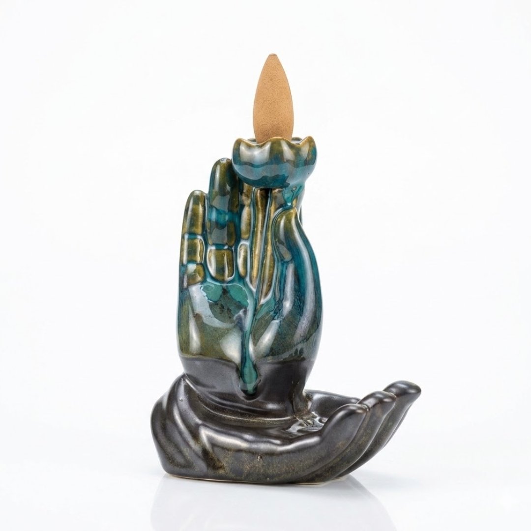 Quemador de incienso cascada de humo en cerámica esmaltada azul y negra con diseño de Mano de Buda sosteniendo una flor de Loto, con un cono de incienso encendido.