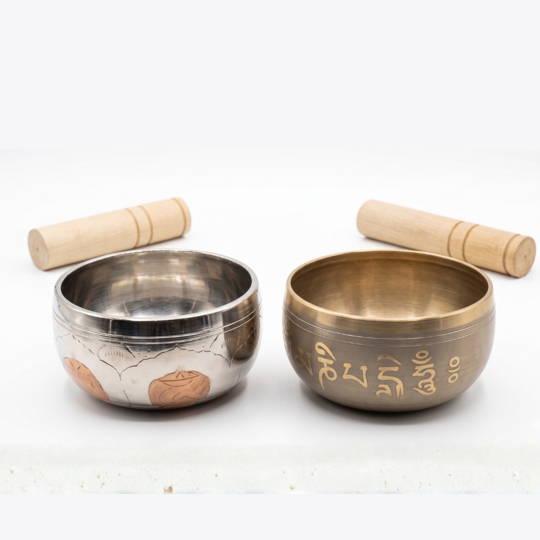 Dos cuencos tibetanos de meditación con sus respectivos mazos de madera; uno plateado con grabados de flor de loto en bronce y otro de bronce patinado con el mantra Om Mani Padme Hum en relieve.